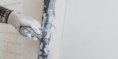 Worker in white gloves performs plastering of the walls of the room